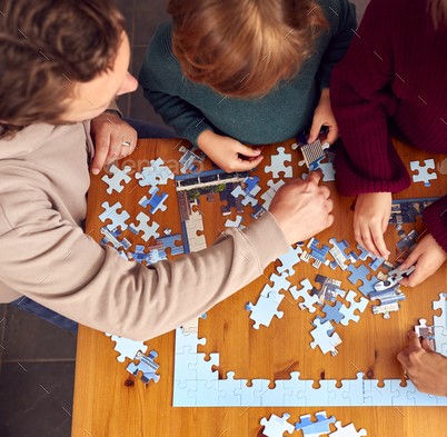 Overhead Shot Of Family Sitting Around Table At Home Doing Jigsaw Puzzle Together